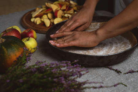 Preparation, celebration of Thanksgiving. Side view. A cook evenly spreads the sugar grains over the surface of the dough for a festive apple pie.の写真素材