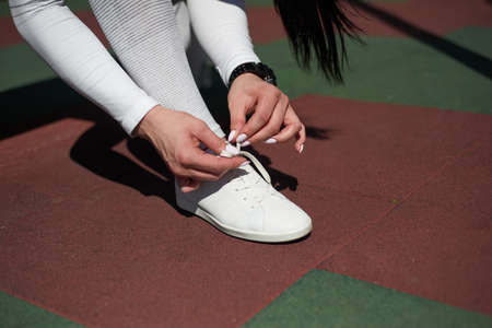 The young woman in a gray tracksuit is tying the laces on her sneakers. Close-up.の写真素材