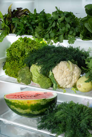 Refrigerator shelves with lots of green vegetables. And half the watermelon on the bottom shelf. Side view. Vegan food.の写真素材