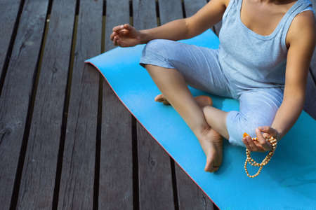 The young woman sits on a mat on a wooden pier in the lotus position. Top view of the legs....