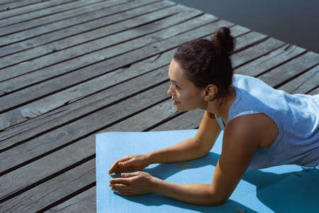 The young woman does a plank exercise on a gymnastic mat and looks in front of her. Side view....