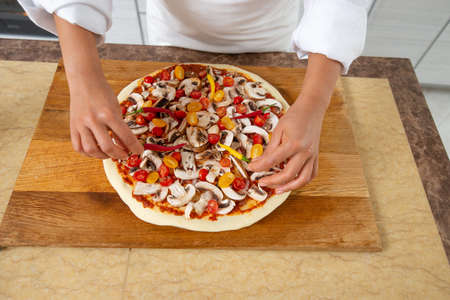Close-up of the chef's hands adding yellow tomatoes to the pizza toppings. Front view. Vegan food.の写真素材