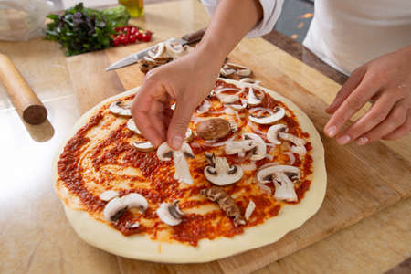 Close-up on the hands of cook laying mushrooms on a pizza. Side view. Vegan food.の写真素材
