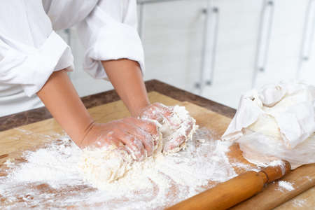 Close-up. A cook kneads the dough with his hands on a wooden board.