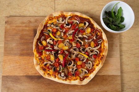 Top view of finished pizza just taken out of the oven. Next is a plate with herbs. Vegan food.の写真素材