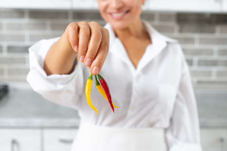 Close-up/ the young woman chef holding hot peppers with fingers.