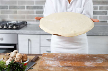 The chef demonstrates a formed pizza dough piece. Close-up.