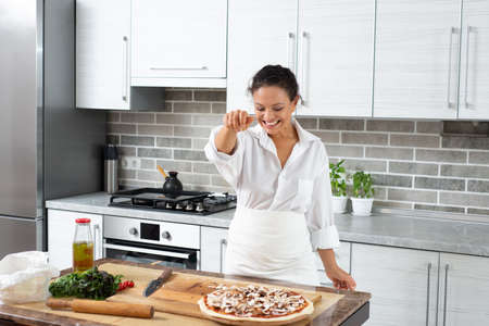 The young woman chef adds toppings to pizza. The chef throws mushrooms on the pizza from above. Cooking vegan pizza.の写真素材