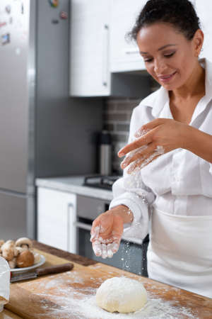 The young woman cook sprinkles flour on the dough.
