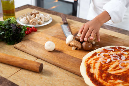 View of the hands of a chef preparing mushrooms for chopping on a wooden board.の写真素材