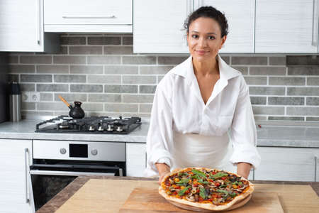 The young woman chef demonstrates ready-to-eat pizza while looking at us. Vegan food.の写真素材