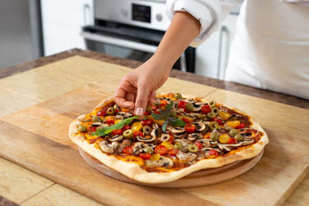 The view of the hands of the chef adding arugula to the finished pizza. Vegan food.の写真素材