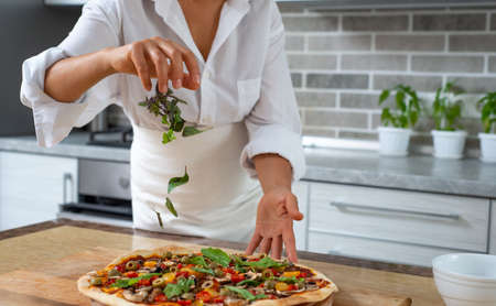 The cook sprinkles the pizza with basil herleavesbs from above. Falling  are visible. Vegan food.