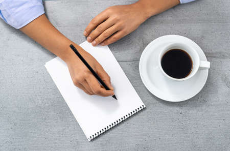 Flat lay of the office space with a view of the hands of a man writing in a notebook, next to a cup of coffee.の写真素材
