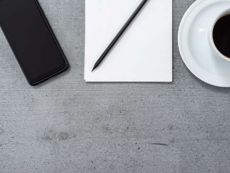 Flat lay of the office space with a view of a smartphone, notepad with a pencil and a cup of coffee.の写真素材