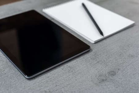 The view of a part of a gray desktop with a view of a tablet and a notebook with a pencil.の写真素材