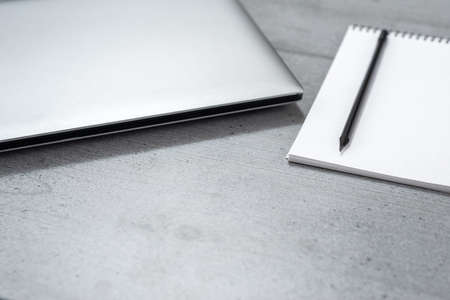 View of the part of a gray desktop with a laptop, notepad and pencil.の写真素材