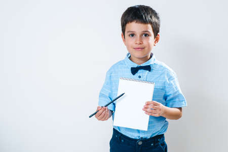 The schoolboy in a shirt with a bow tie holds a notebook in front of him and points at it with a...