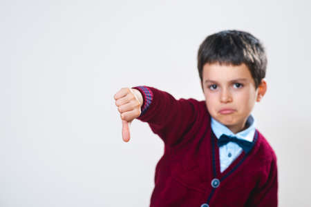 The schoolboy in a sweater shows a thumb down with a negative facial expression. Focus on the hand....