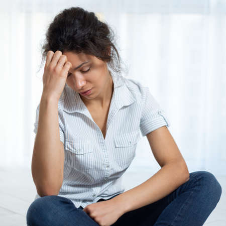 The young woman is sitting on the floor holding her head, having a headache.