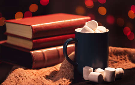 Still life. A cup with marshmallows on a background of colored lights. The stack of books in the background.の写真素材