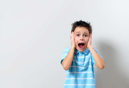 The boy in a blue T-shirt is holding his hands behind his head and screaming.の写真素材