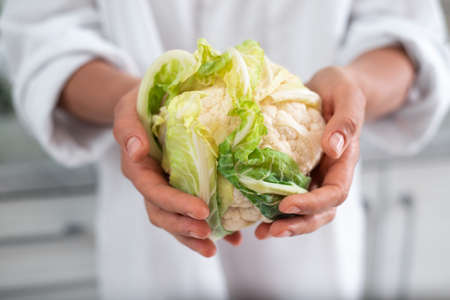 The young female chef shows a camera cauliflower.