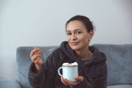 The young woman in good spirits with a lace up hot chocolate with marshmallows staring into the...