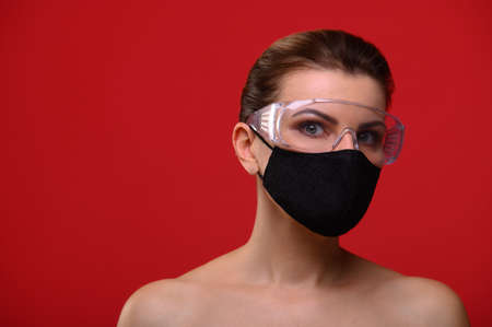The young woman on a red background in protective glasses and a mask.の写真素材