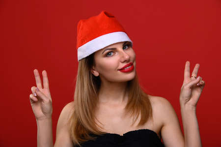 The young woman in a Santa hat smiles and makes quotes with her hands. The concept for the new year and Christmas.の写真素材