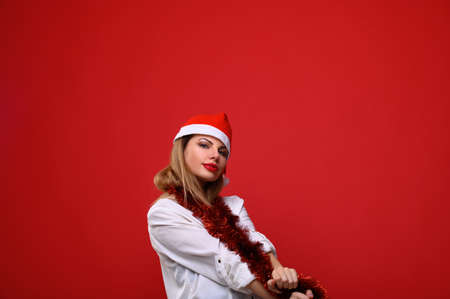 The young woman in Santa's hat with a Christmas tree garland around her neck. The concept for the new year and Christmas.の写真素材