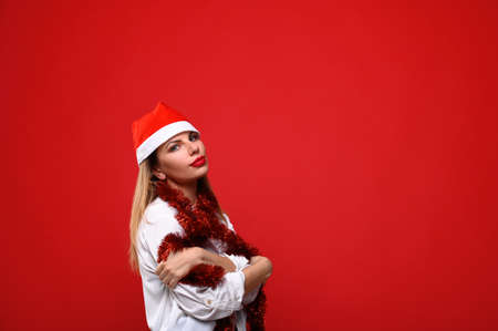 The young woman in Santa's hat with a Christmas tree garland around her neck. The concept for the new year and Christmas.の写真素材