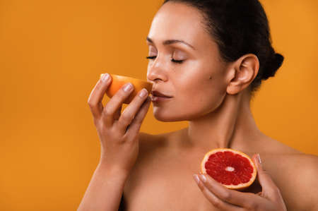 Beaty portrait of a young woman on a yellow background. The woman sniffs a grapefruit.の写真素材