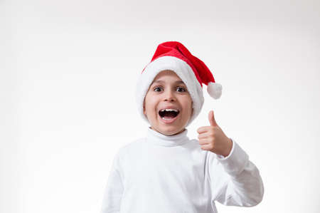 A boy in the red santa hat laughs loudly and shows his thumb. Christmas concept.の写真素材