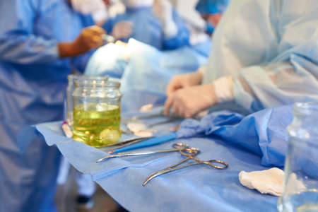 Surgery. In foreground is a table with instruments, in the background, surgeons are performing an...