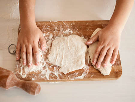 Children's hands lie on top of the dough rolled on a wooden board