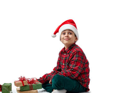 Isolated portrait of the child on white. A boy in a red shirt sits and smiles with his head thrown back, next to Christmas gifts.の写真素材
