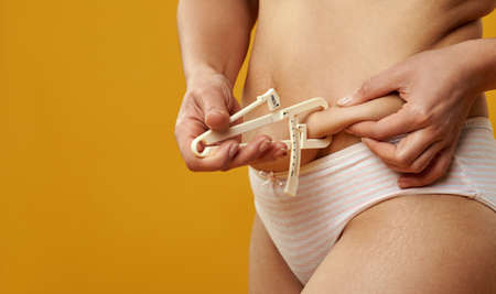 The woman measures the thickness of subcutaneous fat with a fat caliper