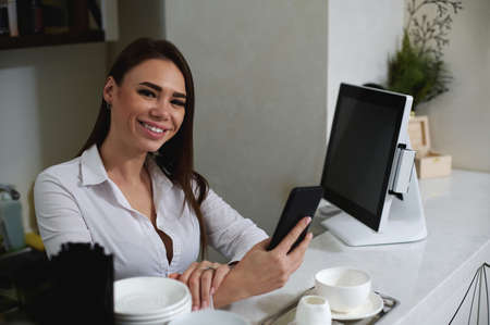 Barista smiles at the camera and holds the phone in her hands