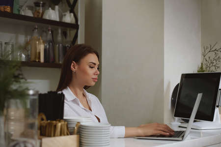 a young caucasian woman works in a laptop behind a bar