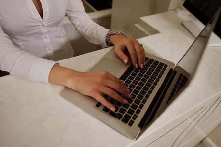 Woman's hands in white shirt typing on laptop keyboard