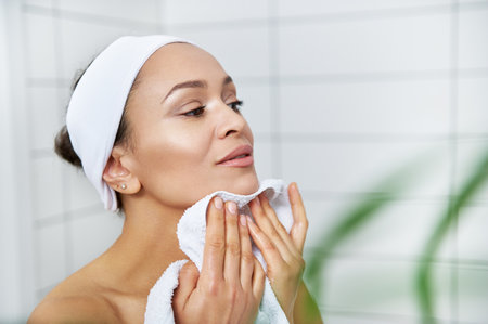 Young beautiful woman wiping her face with white towel in bathroom.の写真素材