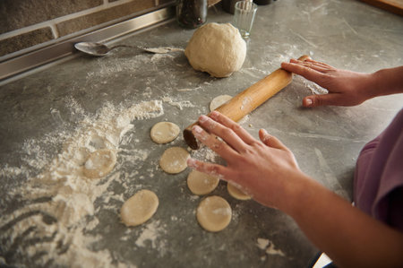 A woman holds a wooden rolling pin. Flour, dough and cut-out shapes for dumplings are sprinkled on...
