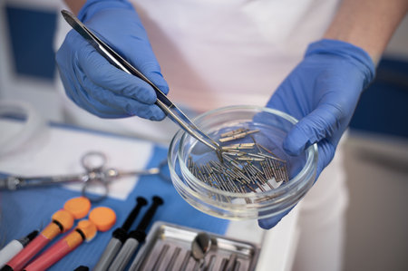 Dentist holding a transparent Petri dish with metal dental drill nozzle burs.