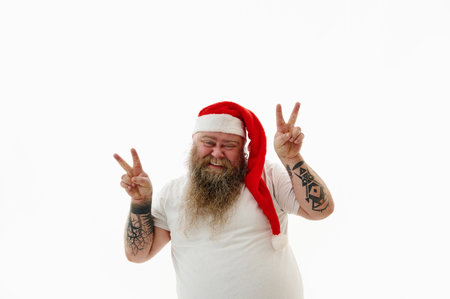An overweigh man in Santa Claus hat doing positive gesture with hands, pointing two finger, smiling and happy for success. Peace signの写真素材