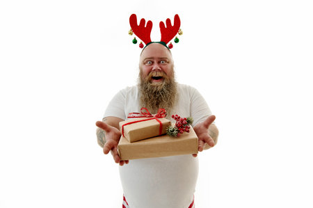 Portrait on a white background of an overweigh man with tattooed arms wearing a hoop with antlers on the head and presenting Christmas gifts.の写真素材
