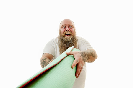 A bearded fat man stretching forward a fitness mat laughinh at camera