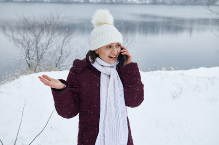 Portrait of a pretty woman wearing white woolen hat and scarf talking on mobile phone on the...