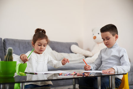 Adorable children sitting at table and drawing using color pencils