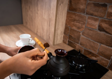 The young woman adds a spoonful of ground coffee to a coffee cup. View of the hands with a spoon.